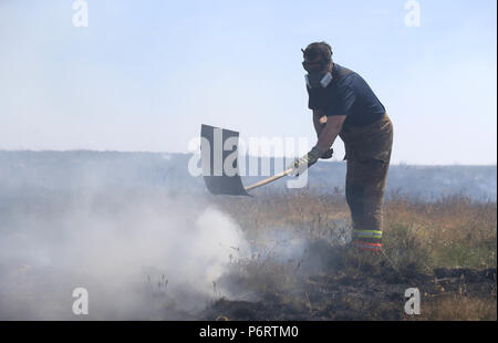 Un vigile del fuoco da Tyne and Wear Fire and Rescue Service mette fuori fuoco sulla collina di inverno vicino a Bolton, come più di 20 motori Fire sono in scena con equipaggio affrontare la brughiera di incendi. Foto Stock