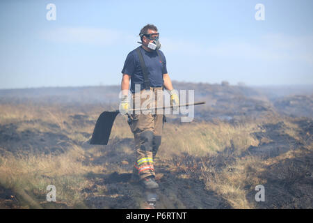 Un vigile del fuoco da Tyne and Wear Fire and Rescue Service mette fuori fuoco sulla collina di inverno vicino a Bolton, come più di 20 motori Fire sono in scena con equipaggio affrontare la brughiera di incendi. Foto Stock