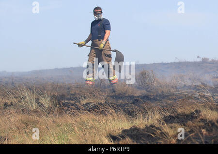 Un vigile del fuoco da Tyne and Wear Fire and Rescue Service mette fuori fuoco sulla collina di inverno vicino a Bolton, come più di 20 motori Fire sono in scena con equipaggio affrontare la brughiera di incendi. Foto Stock