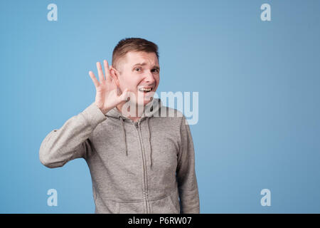 Closeup ritratto di uomo europeo mettendo mano sul orecchio ascoltare con attenzione il gossip isolato sul colore di sfondo blu Foto Stock