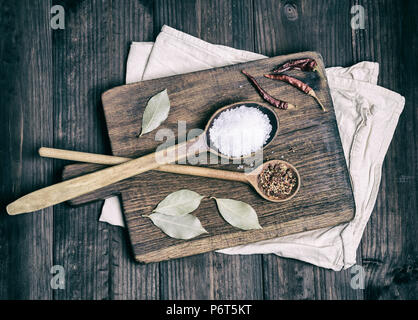 Due cucchiai di legno con spezie e sale bianco su marrone con tagliere, vista dall'alto Foto Stock