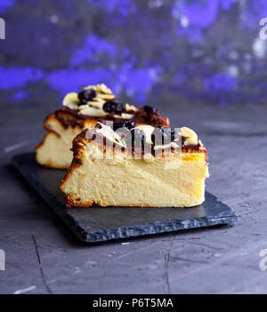 Pezzo di cheesecake su uno sfondo nero cosparso con mandorle a scaglie e asciugare le ciliegie Foto Stock