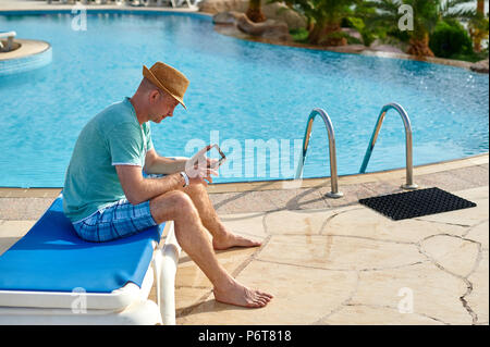 Uomo che utilizza il telefono cellulare in vacanza presso la piscina in hotel, il concetto di un libero professionista che lavora per se stesso su viaggi e vacanze Foto Stock