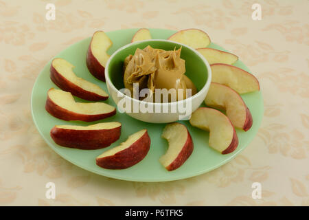 Fette di mela verde snack piastra con piccolo verde ciotola piena di burro di arachidi in centro per immersione Foto Stock