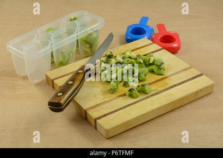 Un trito di materie fresche kiwi sul tagliere di legno e plastica ghiaccioli contenitori per congelamento Foto Stock