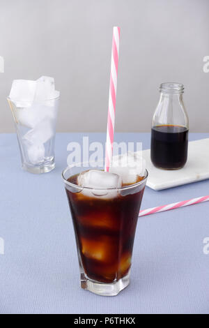 Caffè ghiacciato in un bicchiere con cubetti di ghiaccio e paglia su sfondo viola e una bottiglia di birra fredda caffè concentrato su marmo bianco bordo. Alta vi angolato Foto Stock