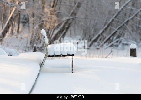 Lonely panchina coperta di spessore neve intatta con frozen river e alberi smerigliato Foto Stock