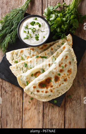 Azerbaijani cibo: flatbread qutab con verdi e yogurt vicino sul tavolo. Verticale in alto vista da sopra Foto Stock