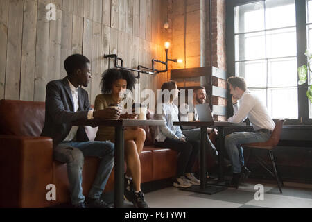Multirazziale millennial godendo di caffè lavorando su gadget in co Foto Stock