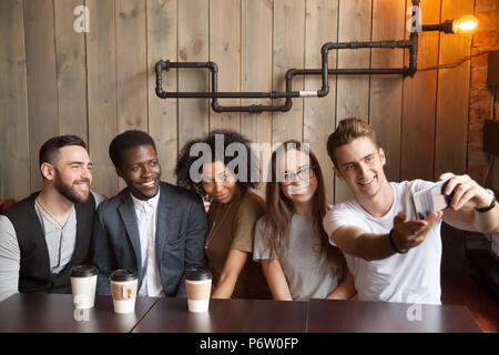 Uomo caucasico prendendo foto di gruppo con diversi amici in cafe Foto Stock