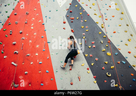 Studente sportivo donna vestita di nero abbigliamento sportivo, salendo sul muro di allenamento in palestra, in vista posteriore Ragazza alleviare lo stress dopo gli esami intensivi tim Foto Stock