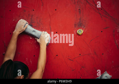 Vista Cropeed di donna scalatore bracci conciate clenching boulder artificiale sulla parete rossa in palestra di arrampicata, closeup shot Foto Stock