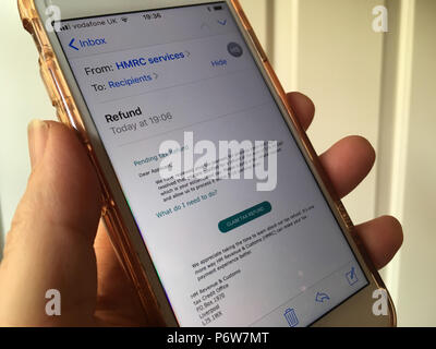 Telefono cellulare nella donna la mano con una truffa / phishing e-mail, che pretendono di essere dall'HMRC, visualizzato sullo schermo Foto Stock