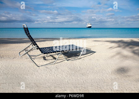 Una sedia vuota di fronte ad una spiaggia di sabbia bianca alla ricerca di una nave da crociera nei Caraibi. Foto Stock