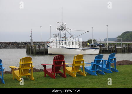 Un array di vivacemente colorate sedie Adirondack affacciato sul porto di Alma, New Brunswick, Canada Foto Stock