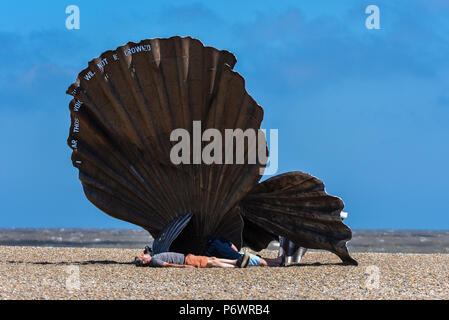 Persone riparo dal forte vento blustery dietro la dentellatura della scultura sulla spiaggia di Aldeburgh. Sebbene sunny un forte vento soffiava dal Mare del Nord. La scultura chiamato smerlo, è dedicata a Benjamin Britten, abituati a camminare lungo la spiaggia nel pomeriggio. Creato da acciaio inossidabile di Suffolk-basato artista Maggi Hambling Foto Stock