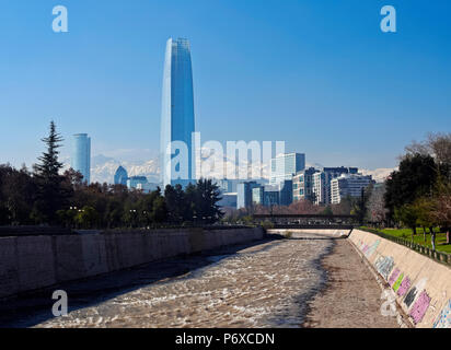 Il Cile, Santiago, vista sul fiume Mapocho, verso l'alto sollevato edifici con Costanera Center Tower, l'edificio più alto in Sud America. Coperta di neve Ande in background. Foto Stock