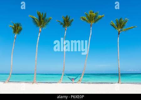 Spiaggia Juanillo (playa Juanillo), Punta Cana, Repubblica Dominicana. Donna relax su una amaca su una spiaggia orlata di palme (MR). Foto Stock