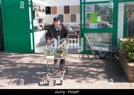 Felice uomo anziano a piedi dal centro giardino con carrello della spesa Foto Stock