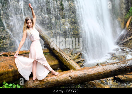 Giovane donna in abito rosa sorge a piedi nudi sul log, le braccia sono sollevate e facendo qualche movimento onirico ed esprimendo happy feeling al Bridal Vei Foto Stock