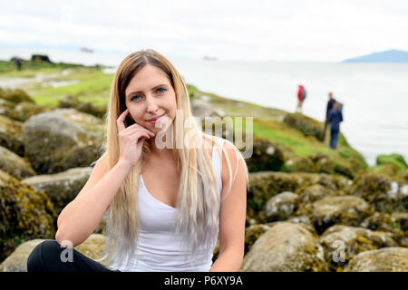 Giovane donna seduta su roccia e sorridente cordiale nella fotocamera in zona intercotidale di Vancouver, British Columbia. Queste rocce sono sott'acqua di Foto Stock