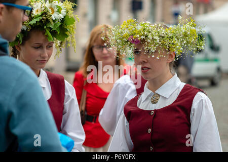 RIGA, Lettonia - 22 giugno 2018: solstizio d'estate mercato. Una giovane donna vestita di un costume nazionale a parlare con i suoi amici. Foto Stock