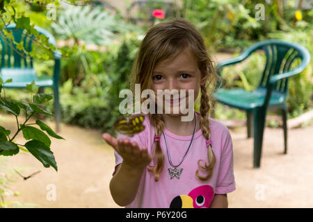 Sorridente ragazza bionda con un giallo maculato butterfly nella sua mano. Medium Shot. Messa a fuoco selettiva. Foto Stock