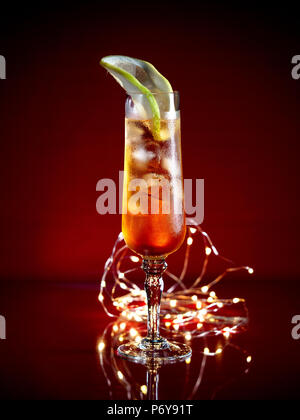 Aperol Spritz guarnito con una fetta di pompelmo servito in un bicchiere alto su sfondo scuro con luci festive Foto Stock