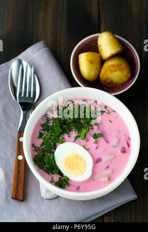 Il lituano Saltibarsciai (Freddo zuppa di barbabietole) con un uovo sodo e le patate di primizia su un sfondo di legno Foto Stock