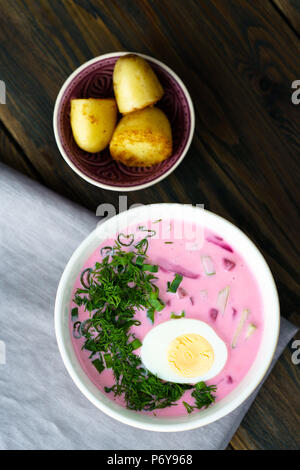 Il lituano Saltibarsciai (Freddo zuppa di barbabietole) con un uovo sodo e le patate di primizia su un sfondo di legno Foto Stock