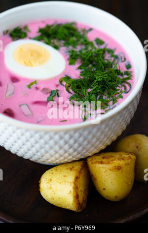Il lituano Saltibarsciai (Freddo zuppa di barbabietole) con un uovo sodo e le patate di primizia su un sfondo di legno Foto Stock