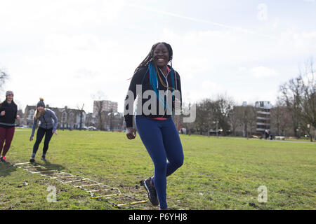 Sorridente, fiducioso donna facendo scala di velocità di punta nel soleggiato parco Foto Stock