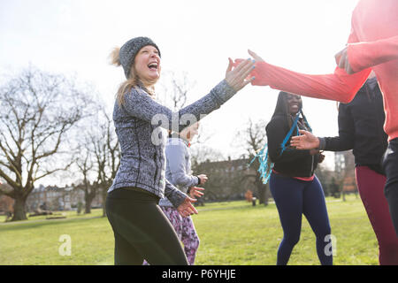 Donna entusiasta di alta fiving classmate, esercitando nel soleggiato parco Foto Stock