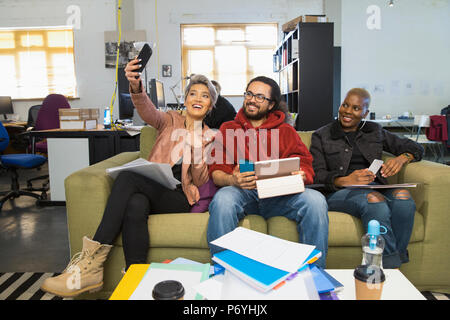 Creative felice la gente di affari tenendo selfie nell'informale aperto ufficio del piano Foto Stock