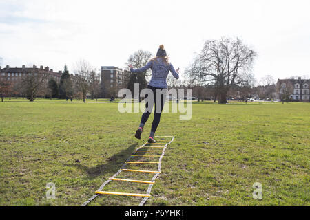 Donna che esercitano, facendo la scaletta di velocità di punta nel soleggiato parco Foto Stock