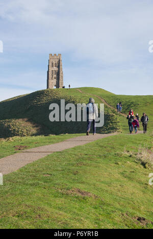 La gente camminare fino al sentiero verso Glastonbury Tor con St Michaels torre contro un cielo blu. Foto Stock