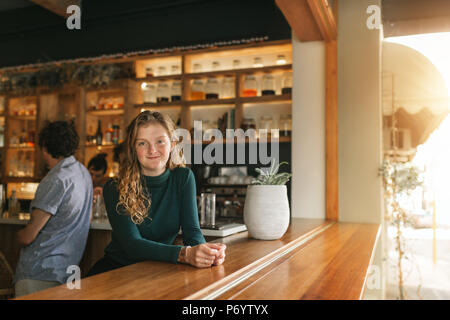 Friendly cameriera appoggiata sul bancone di un bar alla moda Foto Stock