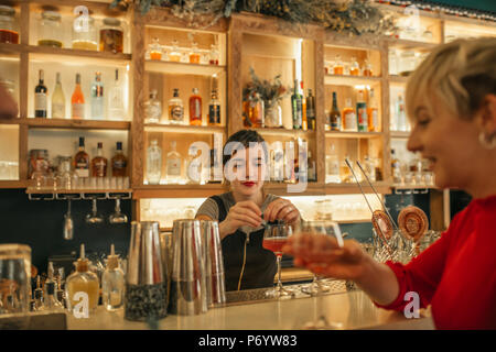 Giovane barista rendendo cocktail dietro un banco di bar Foto Stock