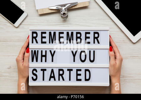 Lo spazio di lavoro con il tablet e smartphone, foglio e 'ricordate il motivo per cui si è iniziato a parole su lightbox su bianco scrivania in legno, vista dall'alto. Mani femminili tenere moderno bo Foto Stock