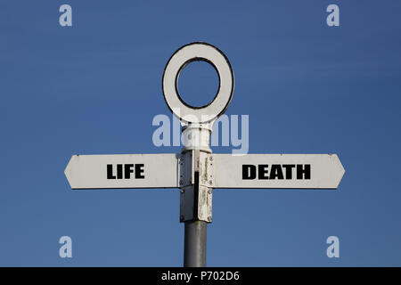 Vecchia strada segno di vita e di morte rivolte in direzioni opposte contro un cielo blu Foto Stock