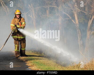 Melbourne, Australia - 13 Aprile 2018: Fire fighter con un tubo flessibile in corrispondenza di una bussola incendio in un'area suburbana di Knox City a est di Melbourne. Foto Stock