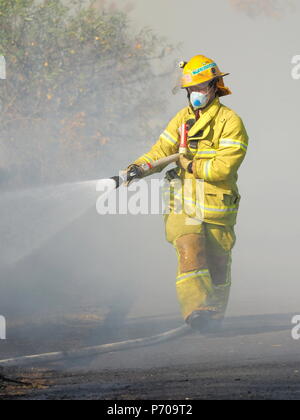 Melbourne, Australia - 13 Aprile 2018: Fire fighter con un tubo flessibile in corrispondenza di una bussola incendio in un'area suburbana di Knox City a est di Melbourne. Foto Stock