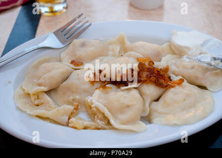 Una piastra di lucidatura tradizionali Pierogi con ripieno di formaggio e patate condito con cipolle fritte e panna acida. Foto Stock