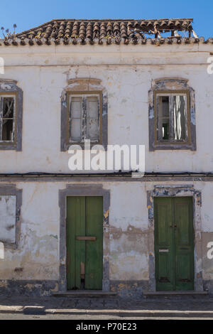 La parte anteriore di una casa abbandonata con la porta verde. Vetri rotti e la caduta del tetto. Azzurro cielo. Castro Marim, Algarve, PORTOGALLO Foto Stock