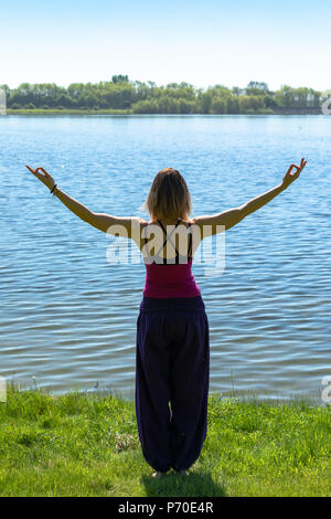 Un istruttore di yoga dimostra lo yoga pone durante un esterno di sessione di yoga in natura con il blu del cielo e colori brillanti. Foto Stock