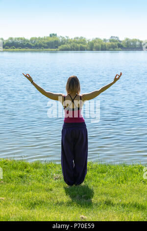 Un istruttore di yoga dimostra lo yoga pone durante un esterno di sessione di yoga in natura con il blu del cielo e colori brillanti. Foto Stock