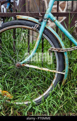 Primo piano di una bicicletta ruota anteriore con una catena e lucchetto appoggiato su di una recinzione arrugginita. Foto Stock