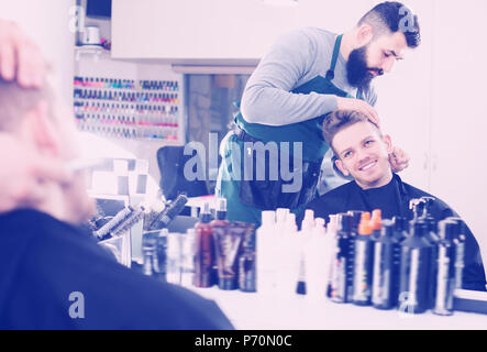 Friendly guy stilista creazione nuova forma per la barba di client al salone di parrucchiere Foto Stock