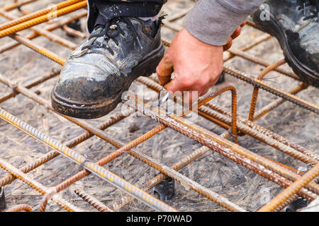 Il lavoratore tiranti in acciaio barre di rinforzo con filo per rafforzare le fondamenta. Close-up. La luce diurna. Foto Stock