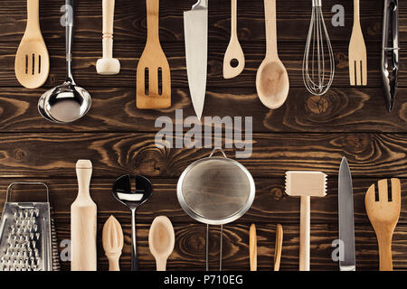 Vista dall'alto di diversi utensili da cucina posti in due righe sul tavolo di legno Foto Stock